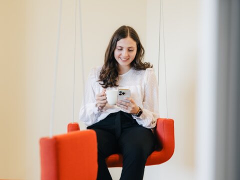 Mitarbeiterin geniesst ihre Pause mit Kaffee und Iphone auf der Büroschaukel. | © instride AG