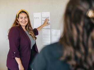 instride Mitarbeiterin Nadja zeigt auf instride.signs in ausgedruckter Version auf Papier und lächelt andere Mitarbeiterin an | © instride AG